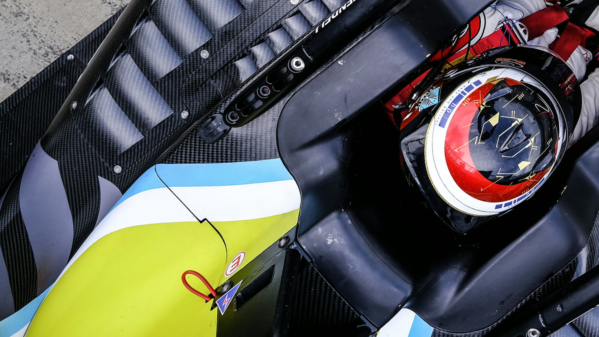 Close-up of the F3 cockpit — the driver's helmet in brand cyan with the TwistStar emblem, carbon bodywork and lime livery.